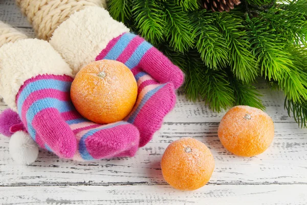 Hands in mittens holding tangerine on wooden background — Stock Photo, Image