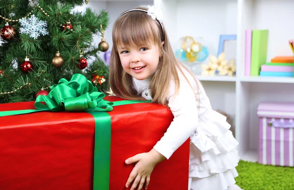 Little girl with big present box near Christmas tree in room — Stock Photo, Image