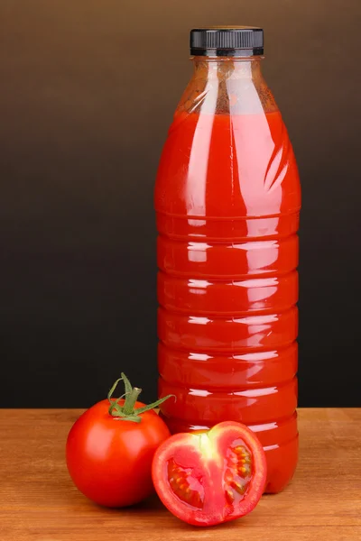 Tomato juice in bottle on wooden table on brown background — Stock Photo, Image