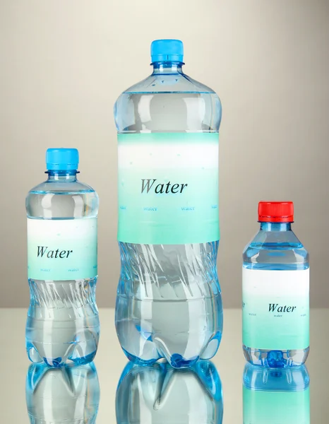 Diferentes botellas de agua con etiqueta sobre fondo gris —  Fotos de Stock