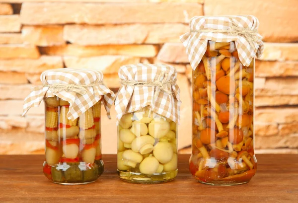 Delicious marinated mushrooms in glass jars, on wooden table on bright background — Stock Photo, Image