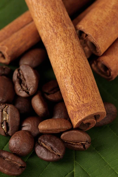 Koffie korrels en kaneel op rouwgewaad op groene blaadjes close-up — Stockfoto