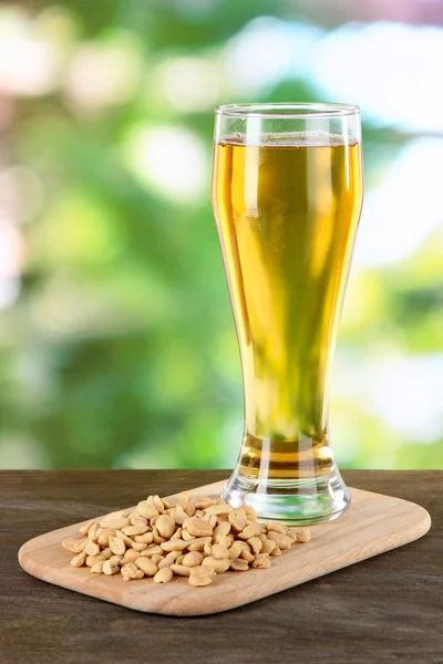 Cerveza en vaso y nueces sobre mesa sobre fondo natural — Foto de Stock