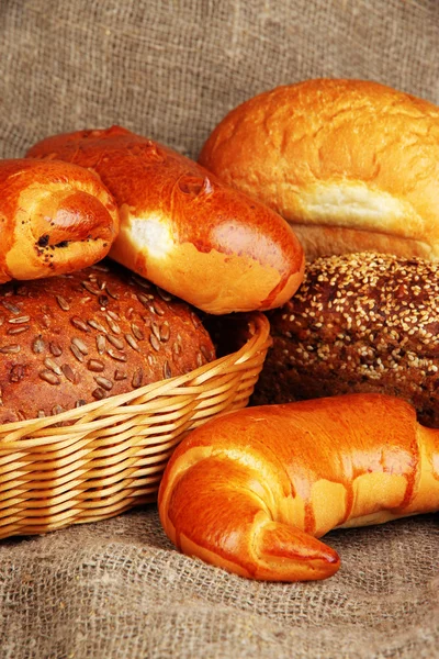 Baked bread in wicker basket on burlap background — Stock Photo, Image