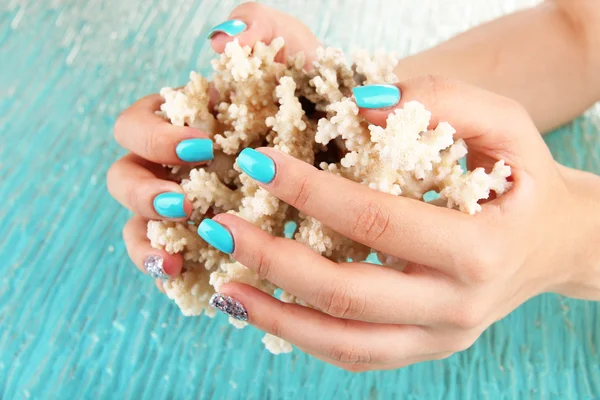 Hermosas manos de mujer con manicura azul sosteniendo coral, sobre fondo de color — Foto de Stock