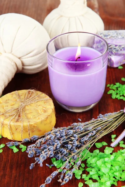 Natura morta con candela alla lavanda, sapone, palle da massaggio, bottiglie, sapone e lavanda fresca, su tavolo in legno su fondo di legno — Foto Stock