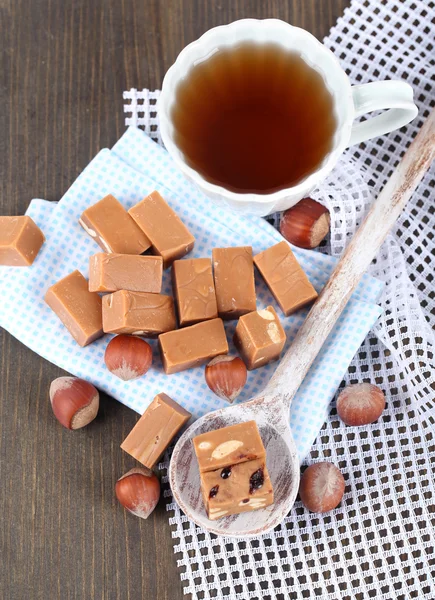 Many toffee in spoon and cup of tea on napkins on wooden table — Stock Photo, Image