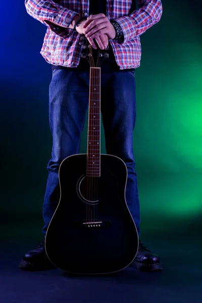 Joven músico con guitarra sobre fondo de color oscuro — Foto de Stock