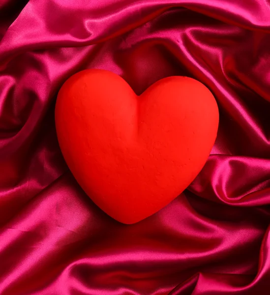 Декоративное красное сердце, на фоне цветной ткани — стоковое фото