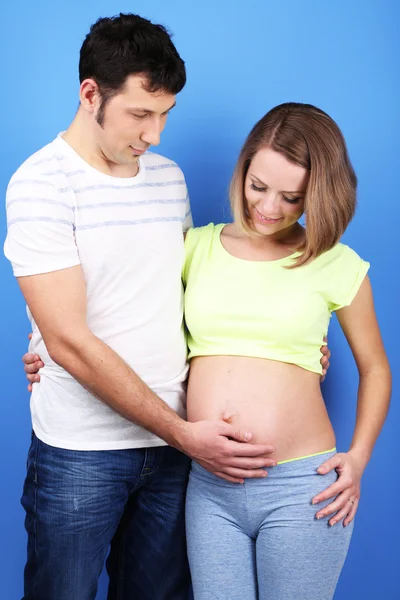 Jonge zwangere vrouw met haar echtgenoot op blauwe achtergrond — Stockfoto