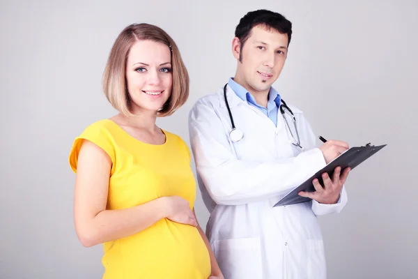 Mujer embarazada joven con médico sobre fondo gris — Foto de Stock