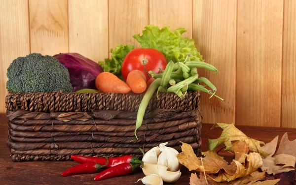 Different vegetables in basket with yellow leaves on table on wooden background — Stock Photo, Image