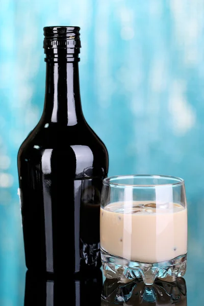 Baileys liqueur in bottle and glass on blue background — Stock Photo, Image