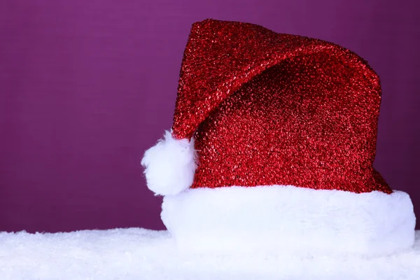 Sombrero de Santa sobre nieve sobre fondo púrpura —  Fotos de Stock