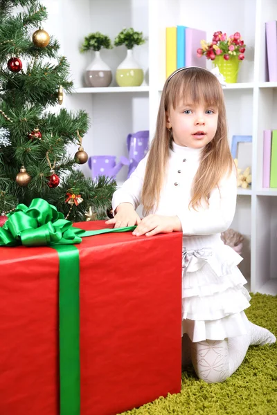 Niña con caja de regalo grande cerca del árbol de Navidad en la habitación —  Fotos de Stock