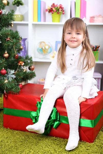 Niña ajuste en la caja de regalo grande cerca del árbol de Navidad en la habitación —  Fotos de Stock