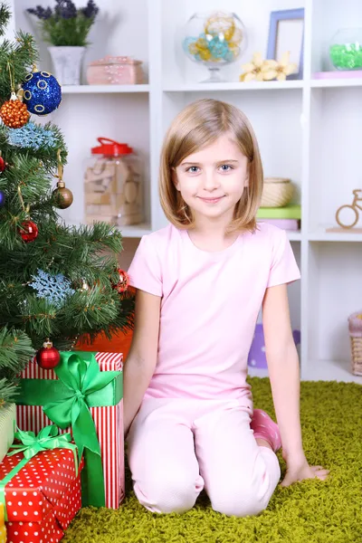 Menina sentada perto da árvore de Natal no quarto — Fotografia de Stock