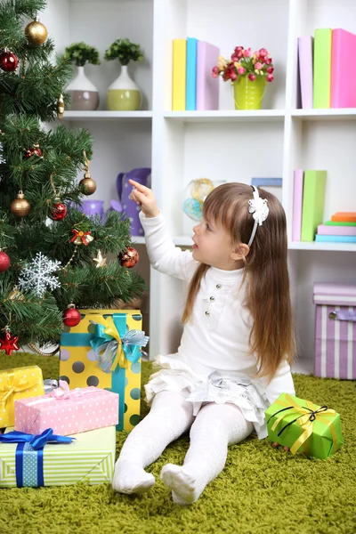 Little girl with present box near Christmas tree in room Royalty Free Stock Images