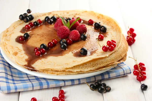 Delicious pancakes with berries and chocolate on plate on wooden table — Stock Photo, Image