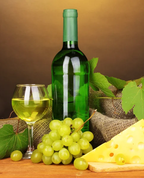 Garrafa de grande vinho com vidro e queijo em mesa de madeira sobre fundo marrom — Fotografia de Stock