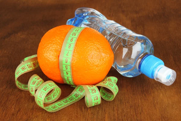 Orange with measuring tape, bottle of water, on wooden background — Stock Photo, Image