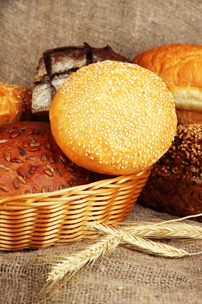 Baked bread in wicker basket on burlap background — Stockfoto