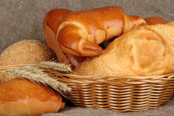 Baked bread in wicker basket on burlap background — Stock Photo, Image