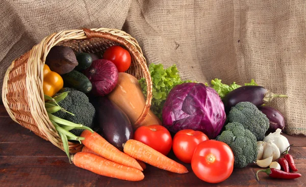 Diferentes verduras en cesta en la mesa sobre fondo de saco —  Fotos de Stock