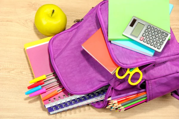 Purple backpack with school supplies on wooden background — Stock Photo, Image