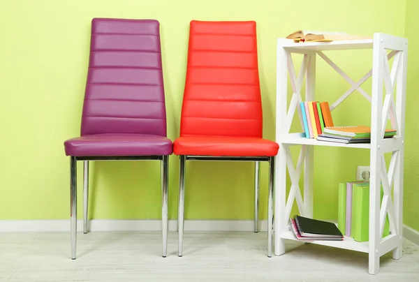 Interior bonito com cadeiras de cor moderna, livros em suporte de madeira, no fundo da parede — Fotografia de Stock