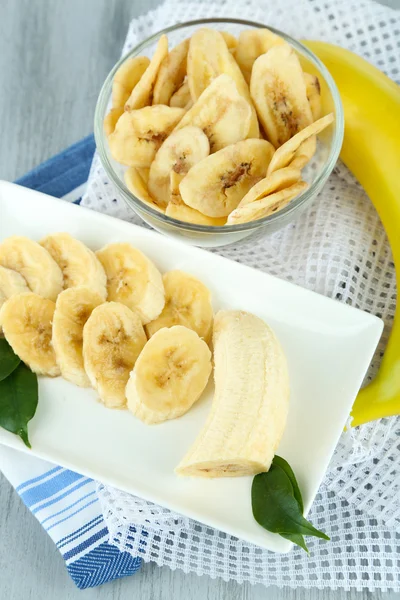 Fresh and dried banana slices on plate, on cutting board, on wooden background — Stock Photo, Image