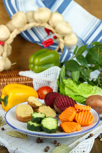 Beaux légumes tranchés, sur assiette, sur fond de bois — Photo