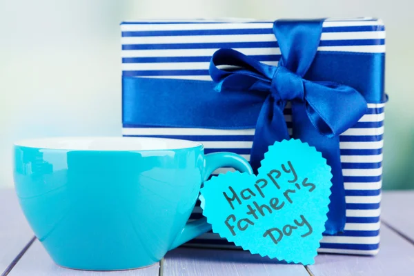 Happy Fathers Day tag with gift box and cup, on wooden table, on light background — Stock Photo, Image