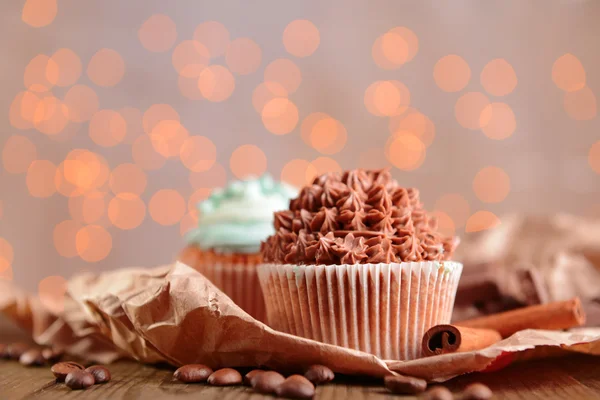 Cupcakes saborosos com creme de manteiga, na mesa de madeira, no fundo luzes — Fotografia de Stock
