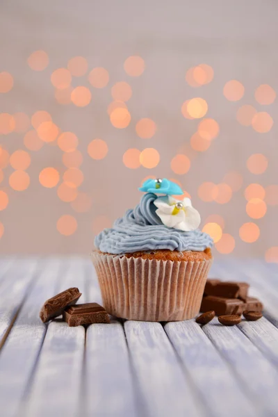 Sabroso cupcake con crema de mantequilla, sobre tabla de madera de color, sobre fondo de luces —  Fotos de Stock