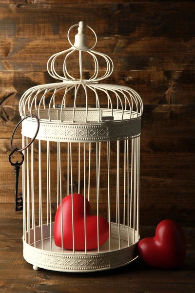 Hearts in decorative cage on wooden background — Stock Photo, Image