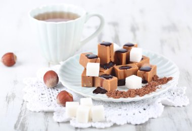 Many toffee on plate and cup of tea on napkin on wooden table clipart