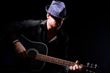 genç müzisyen akustik gitar çalıyor ve şarkı söyleme, koyu arka plan üzerinde