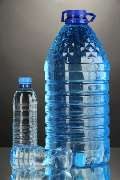 Diferentes garrafas de água no fundo cinza — Fotografia de Stock