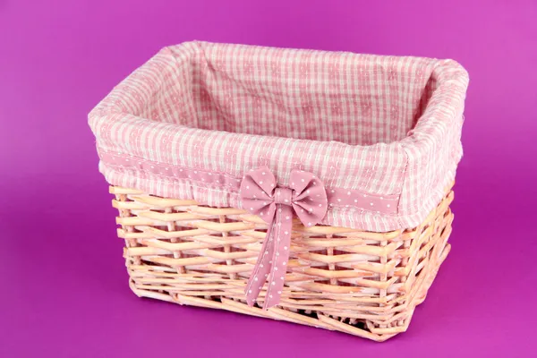 Wicket basket with pink fabric and bow, on color background — Stok fotoğraf