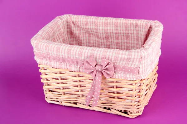 Wicket basket with pink fabric and bow, on color background — Stock Photo, Image