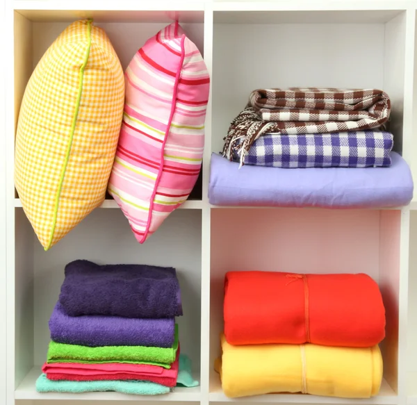 Bright pillows, towels and plaids on shelves, isolated on white — Stock Photo, Image