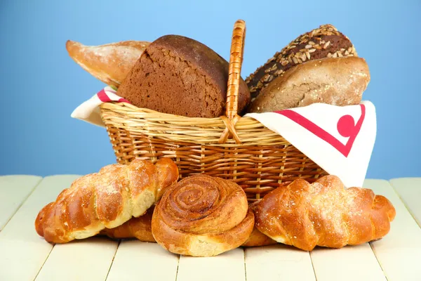 Composizione con pane e panini, in cesto di vimini su tavolo di legno, su sfondo a colori — Foto Stock