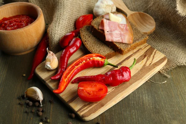 Sammansättning med salsa sås på vitlök, på säckväv, på trä bakgrund,, red hot chili peppers och bröd — Stockfoto