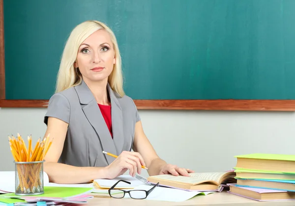 Professora da escola sentada à mesa no fundo do quadro negro — Fotografia de Stock