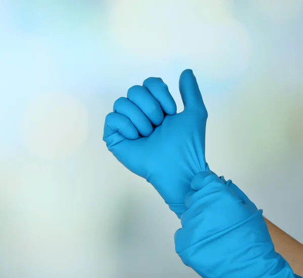 Doctor putting on protective gloves, on light background — Stock Photo, Image