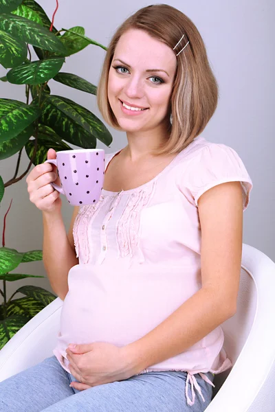 Jeune femme enceinte assise sur un fauteuil et tenant une tasse à la maison — Photo