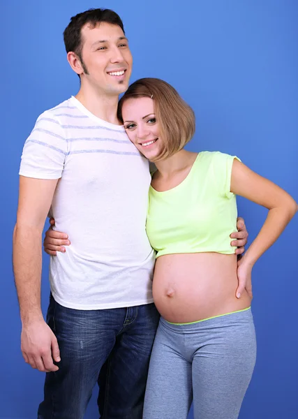 Jovem grávida com o marido no fundo azul — Fotografia de Stock