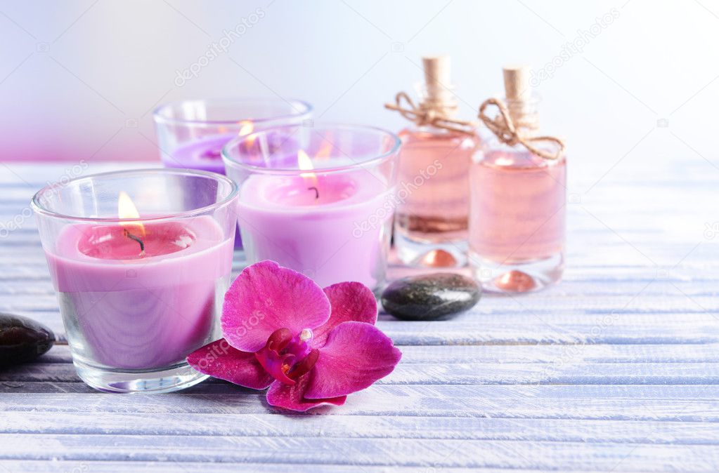 Beautiful colorful candles, spa stones and orchid flower,on color wooden table, on light background
