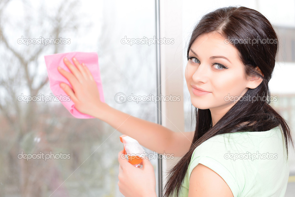Beautiful young woman washing window in room